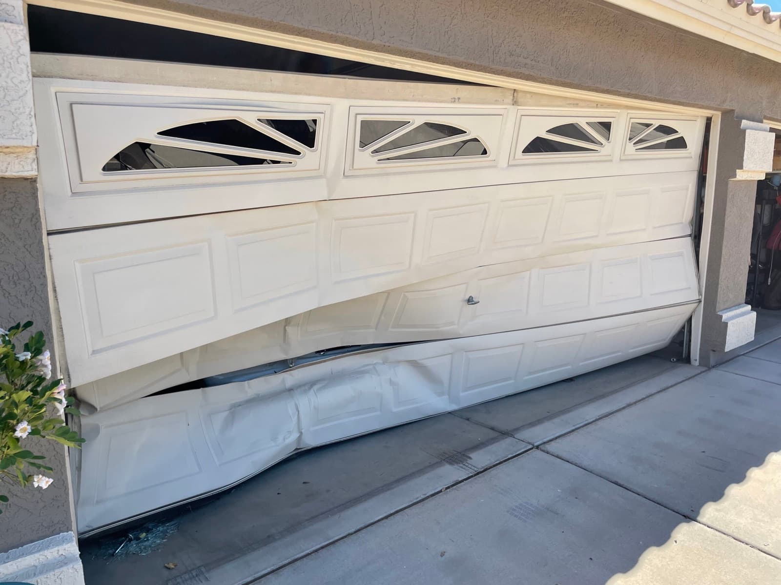 A damaged garage door on a stucco Phoenix-area home, buckled and off its track