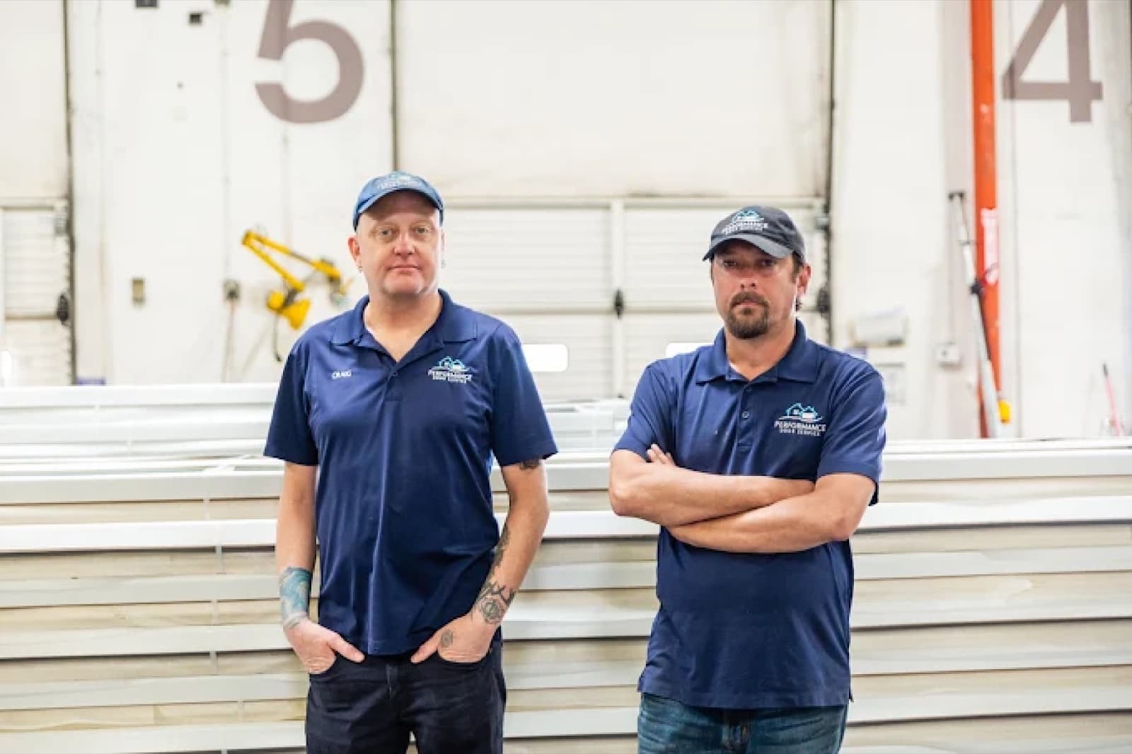 Two Performance Door Service technicians in the warehouse in front of stacked garage door panels